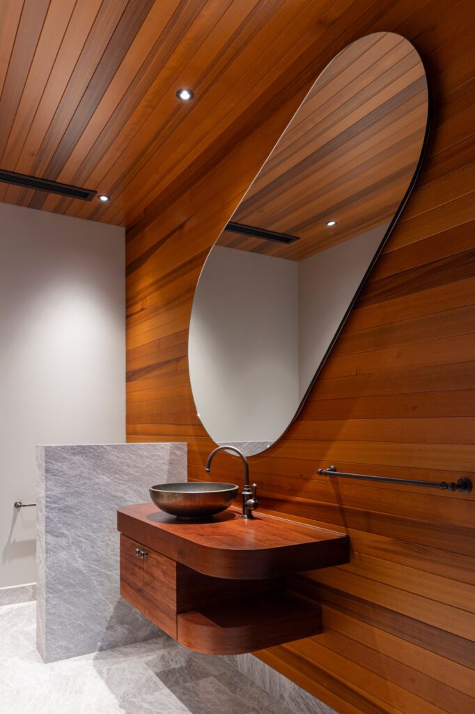 Timber-clad powder room with a sculptural vanity and oval mirror